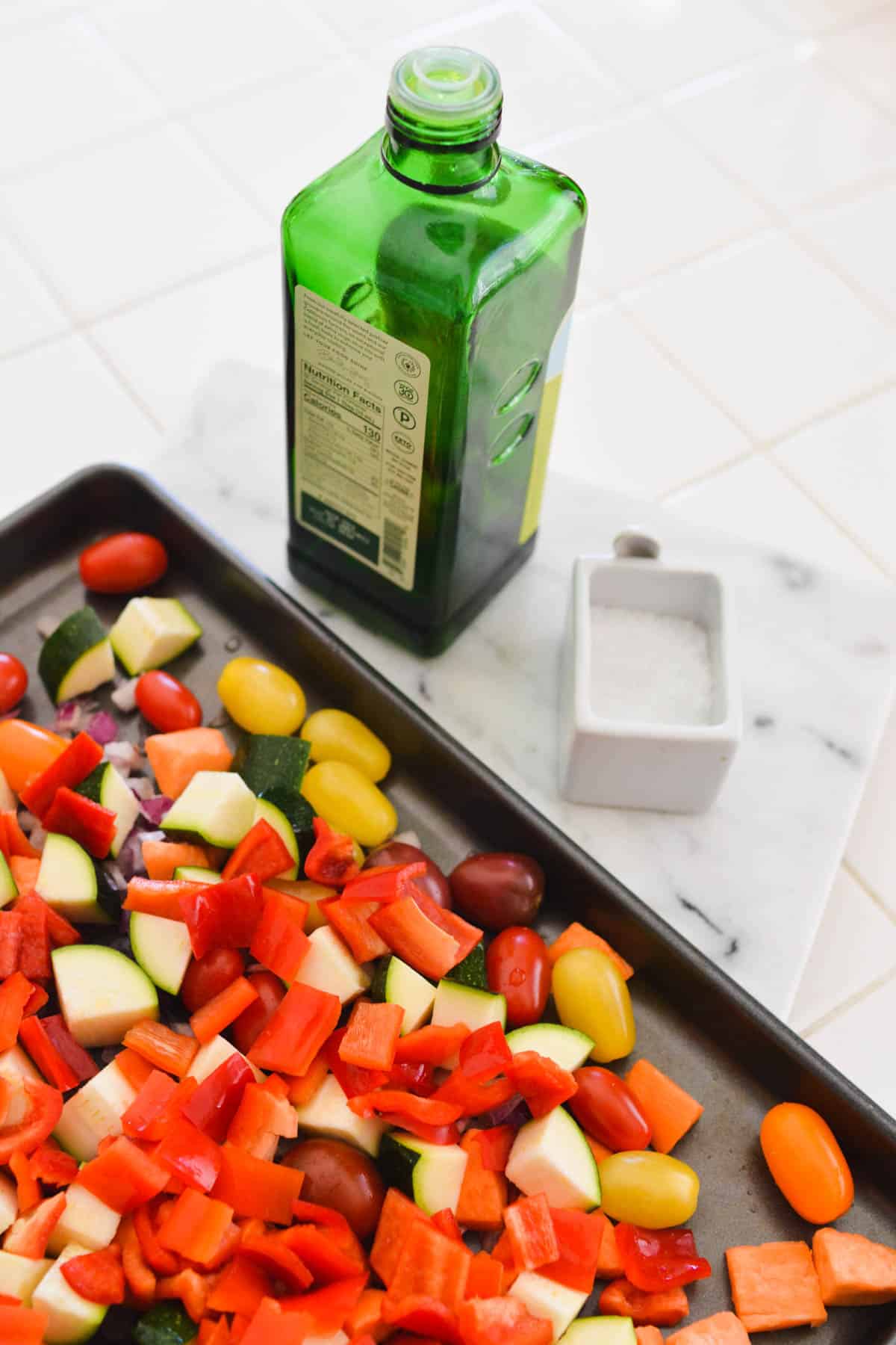 Cut up vegetables on a sheet pan next to a bottle of olive oil.