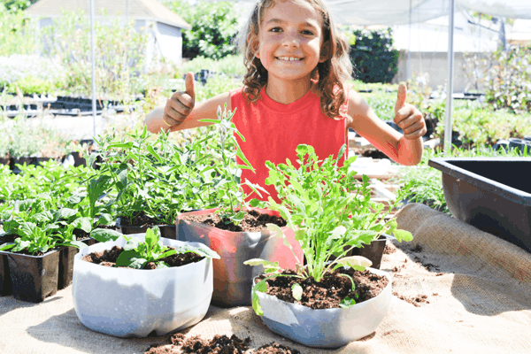 Kid standing by his milk jug garden.