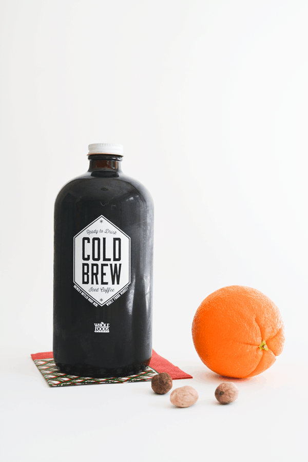 A bottle of cold brew, an orange and some spices on a table. 