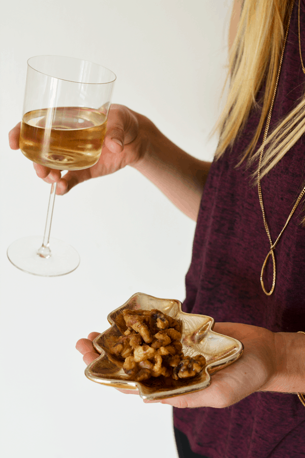 Girl holding dish of cinnamon walnuts in one hand and a glass of wine in the other.