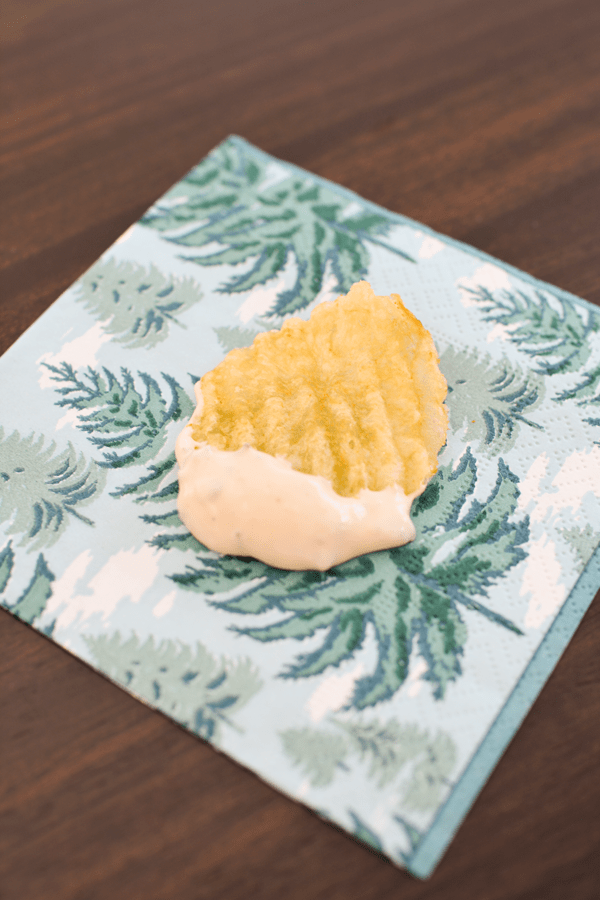 A ruffled potato chip on a decorative napkin that has been dipped into dip.