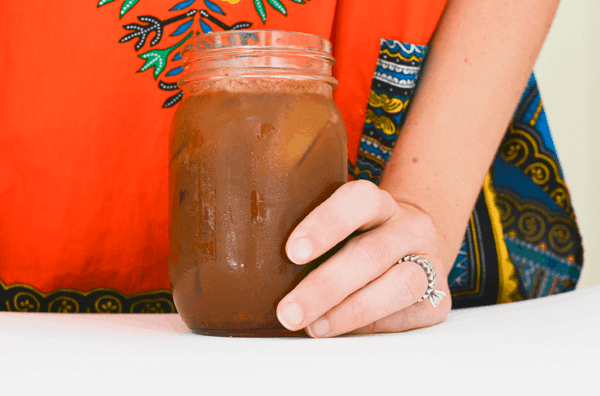 Woman holding on to a jar of iced coffee on a table. 