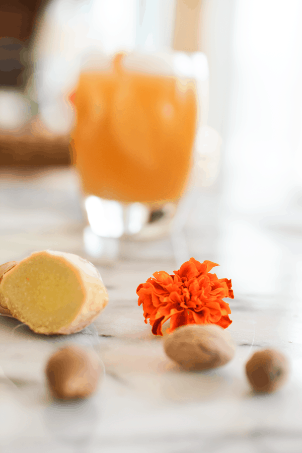 Fresh ginger and nutmeg on a cutting board next to an orange marigold. 