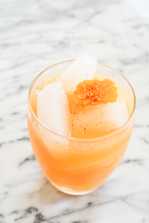Overhead shot of a pear cocktail on a marble table topped with fresh nutmeg and a marigold. 