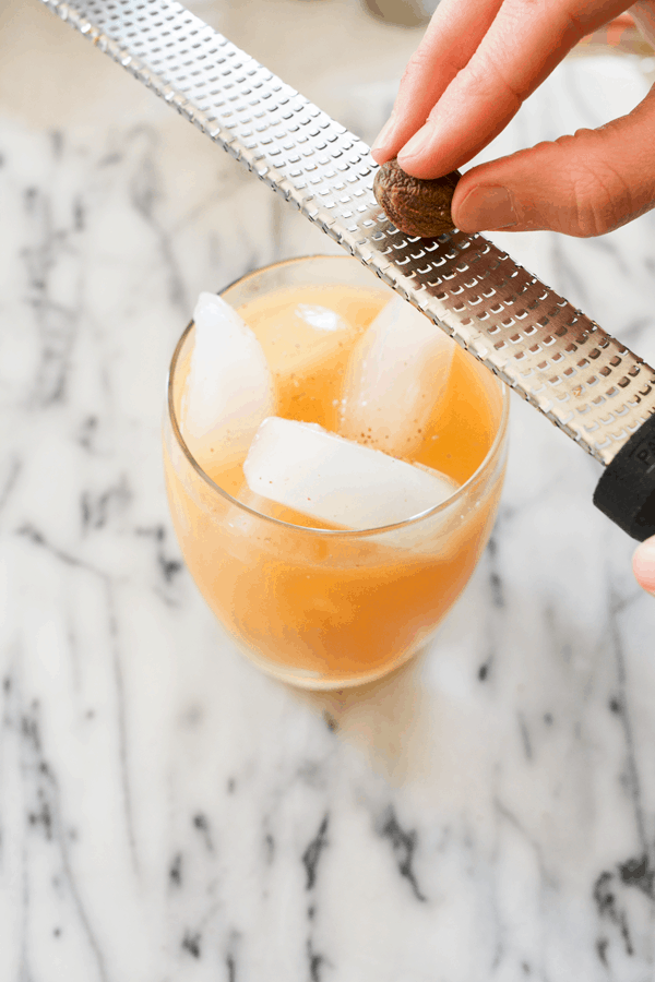 A cocktail sitting on a marble table with someone grating fresh nutmeg on top.