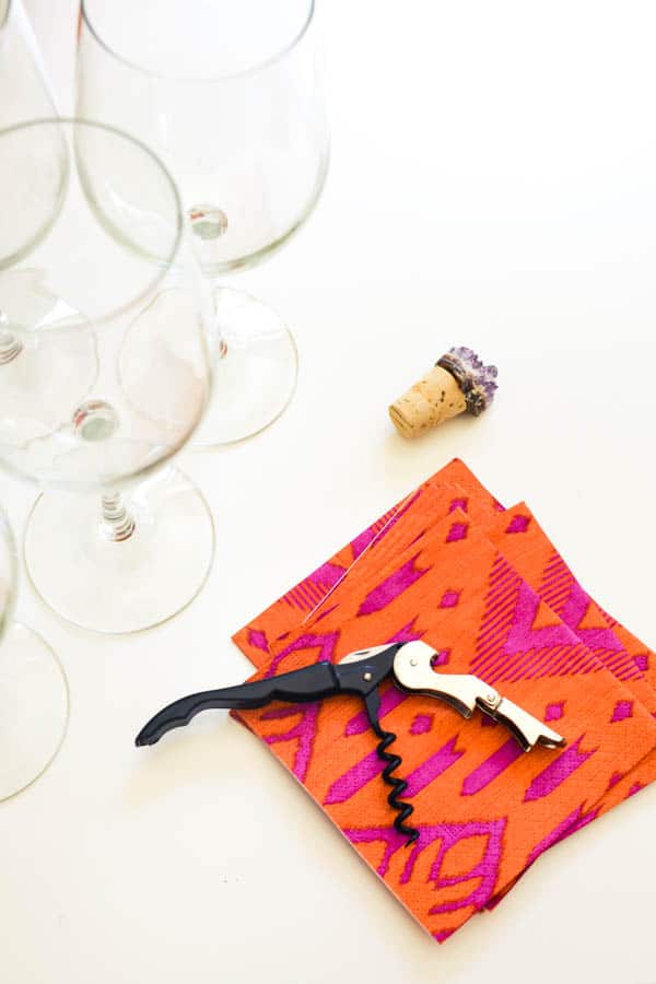Wine cork and bottle opener on top of festive napkins next to wine glasses. 