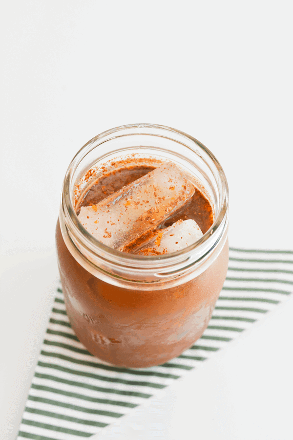 Close up of a jar with iced coffee topped with orange zest and fresh nutmeg. 