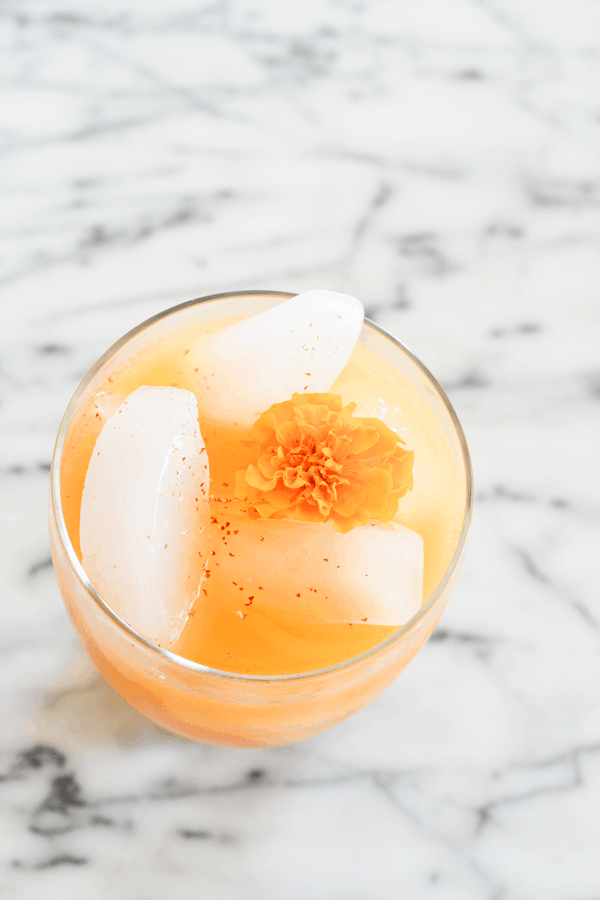 Overhead view of an orange cocktail on a marble table topped with an orange marigold.