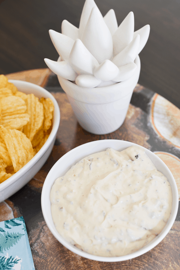 Bowl of dip on a tray next to potato chips.