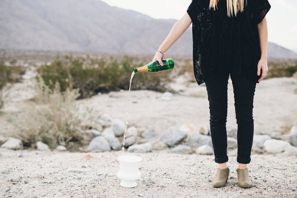 Woman standing and pouring champagne into a white punch bowl on the ground. 