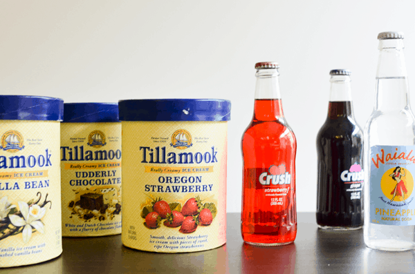 Cartons of ice cream next to bottles of flavored soda on a wood countertop.