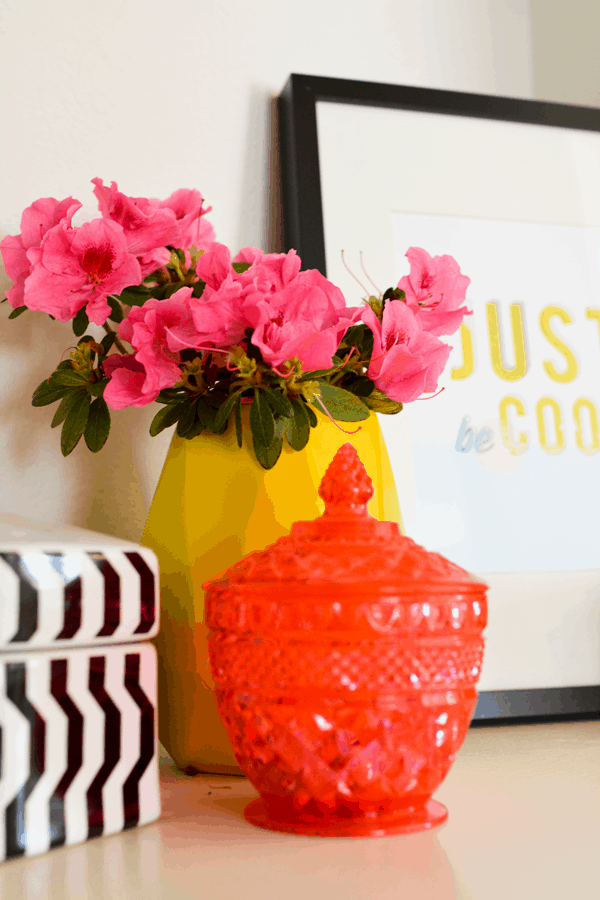 hot pink candy dish next to a yellow vase with pink flowers on a shelf