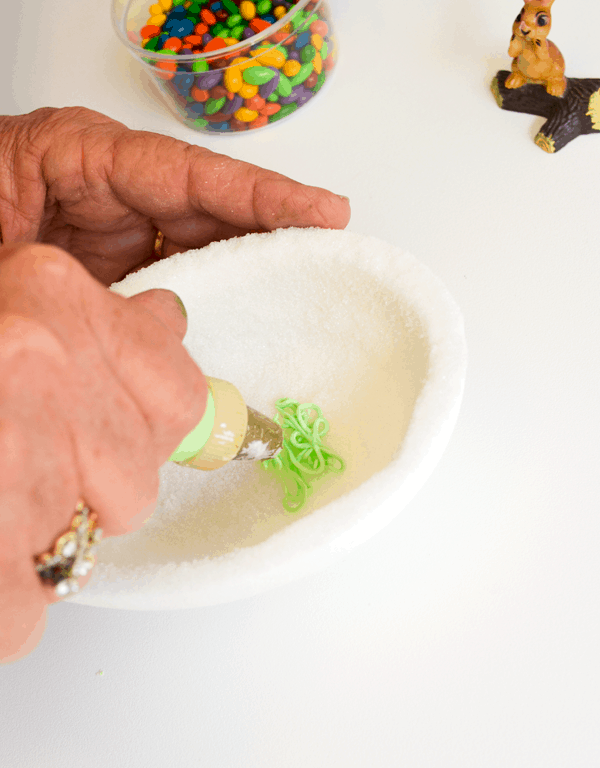 Woman adding green frosting grass to the inside of a white sugar Easter egg.
