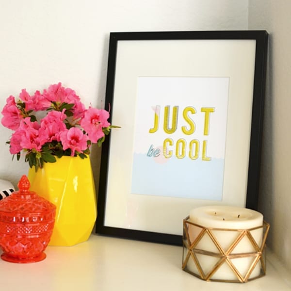 A vase of flowers on a table next to framed art and a candle.