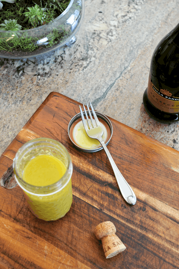 A jar of prosecco vinaigrette dressing on a cutting board with a fork resting on the lid.