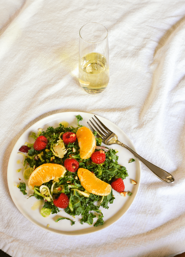 Kale salad with Prosecco vinaigrette on a plate topped with oranges and raspberries.