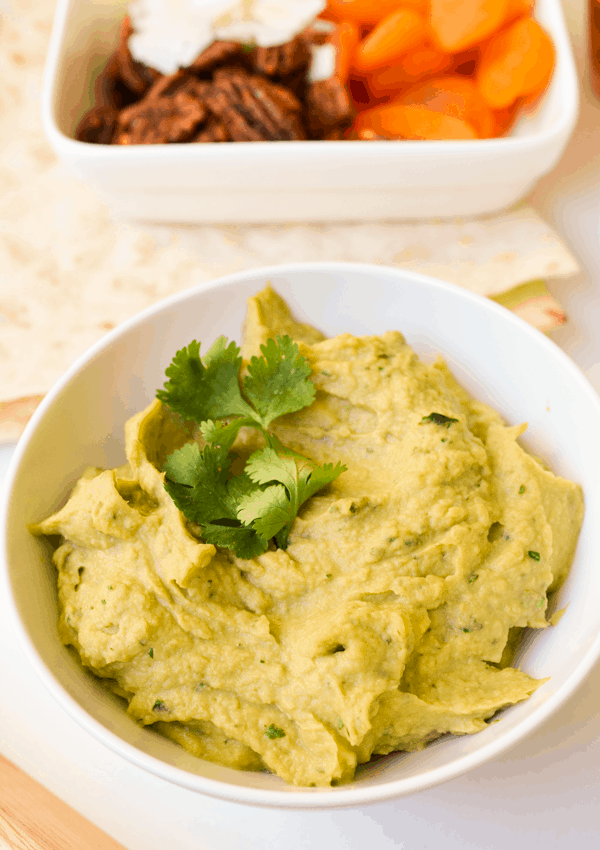 Avocado hummus in a white bowl topped with cilantro leaves.