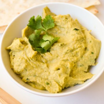 Close up of a white bowl holding a portion of spicy Avocado Hummus topped with cilantro.