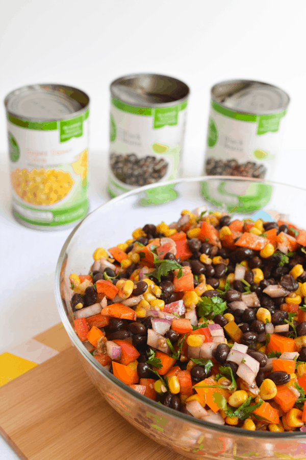 A bowl of chopped veggies with black beans and cilantro with empty cans in the background.