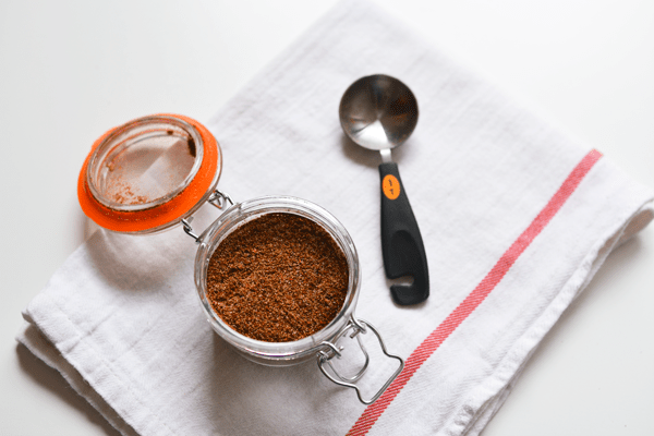 Glass jar filled with seasoning on a towel next to a measuring spoon. 