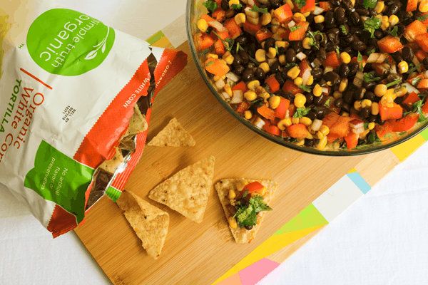 Bowl with black ban salad on a cutting board next to a bag of tortilla chips.