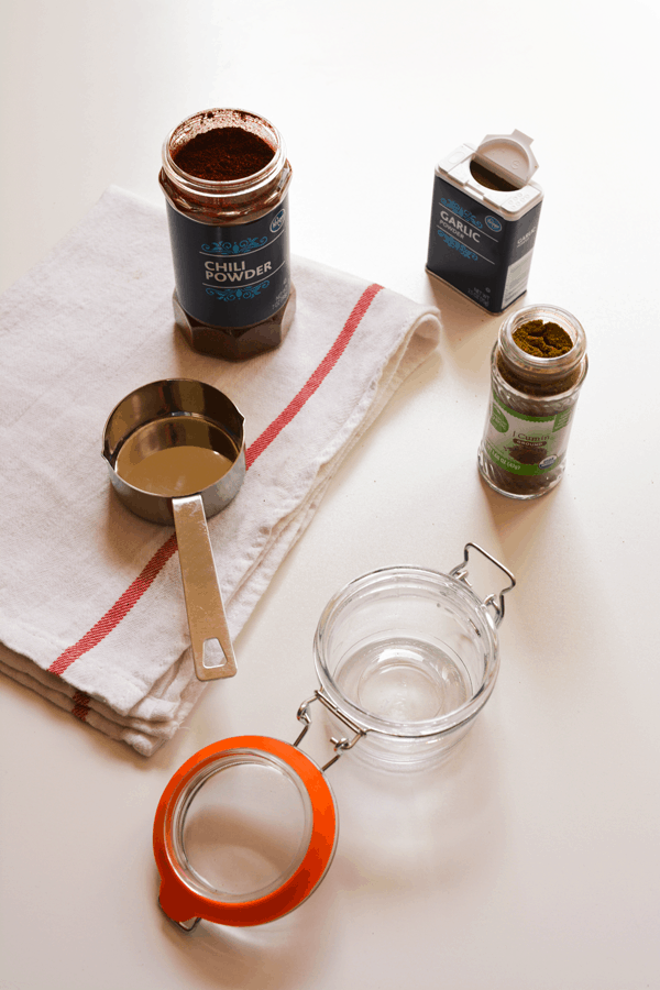 Containers of spices on a table next to a measuring spoon and glass canister.