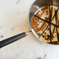 Vanilla beans and cinnamon sticks infusing a saucepan of simple syrup.