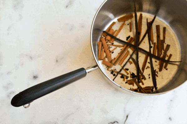 Vanilla beans and cinnamon sticks infusing a saucepan of simple syrup.