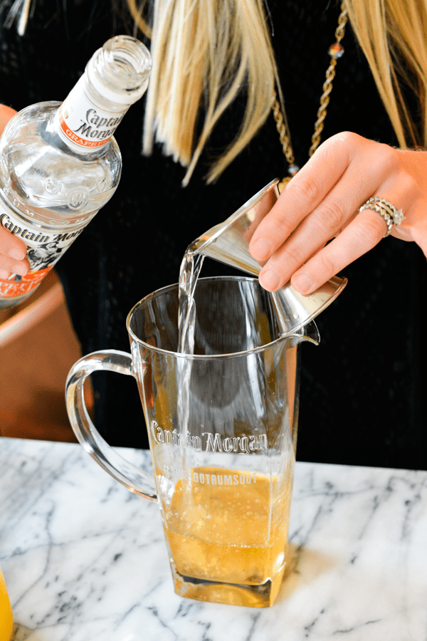 Woman measuring rum with a jigger and adding it to a pitcher.