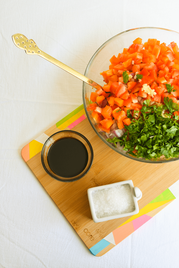 A bowl of balsamic vinegar and cellar of sea salt on a cutting board next to a bowl with chopped veggies and cilantro.