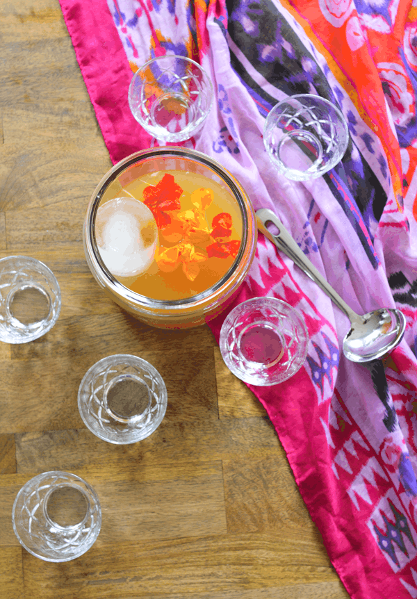 Rum punch in a punch bowl and topped with edible flowers next to cups and a ladel.