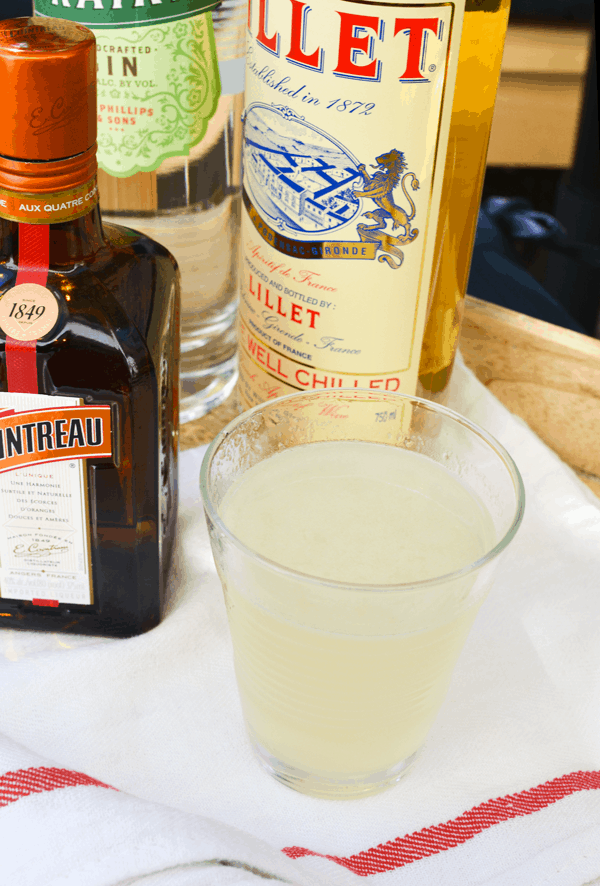 Close up of a Corpse Reviver cocktail in a glass next to a bottle of Lillet and Cointreau. 