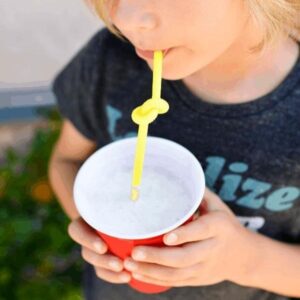 Kid holding a red plastic cup with bendy straw in his mouth.
