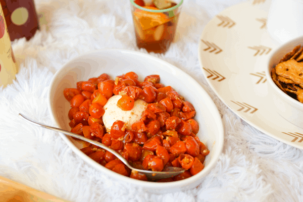 Roasted garlic cherry tomatoes with burrata cheese in a dish on a white furry blanket as an easy appetizer idea. 