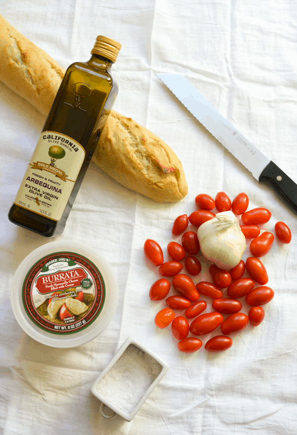 Ingredients to make a burrata appetizer recipe with roasted tomatoes on a white linen.