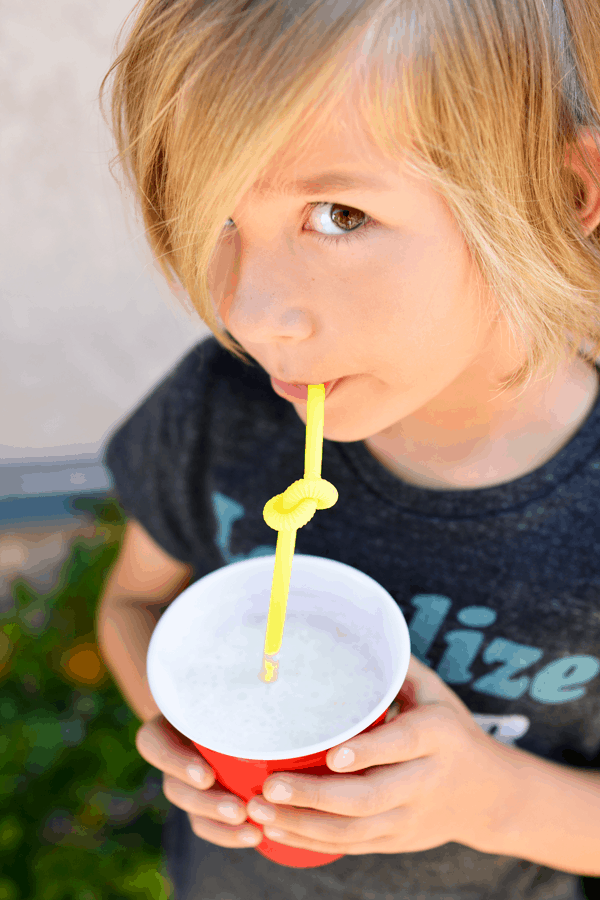 Pina Colada Slush mocktail being drunk by a child out of a red solo cup with a yellow curly straw.