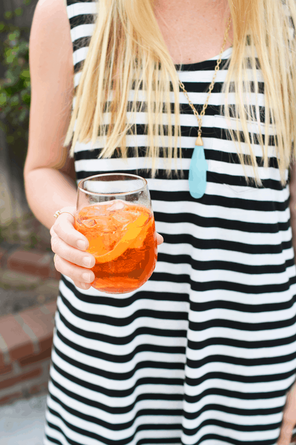 A girl in a black and white striped dress holding an Aperol Spritz cocktail 