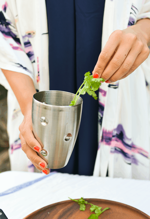 Woman adding cilantro to a cocktail shaker.