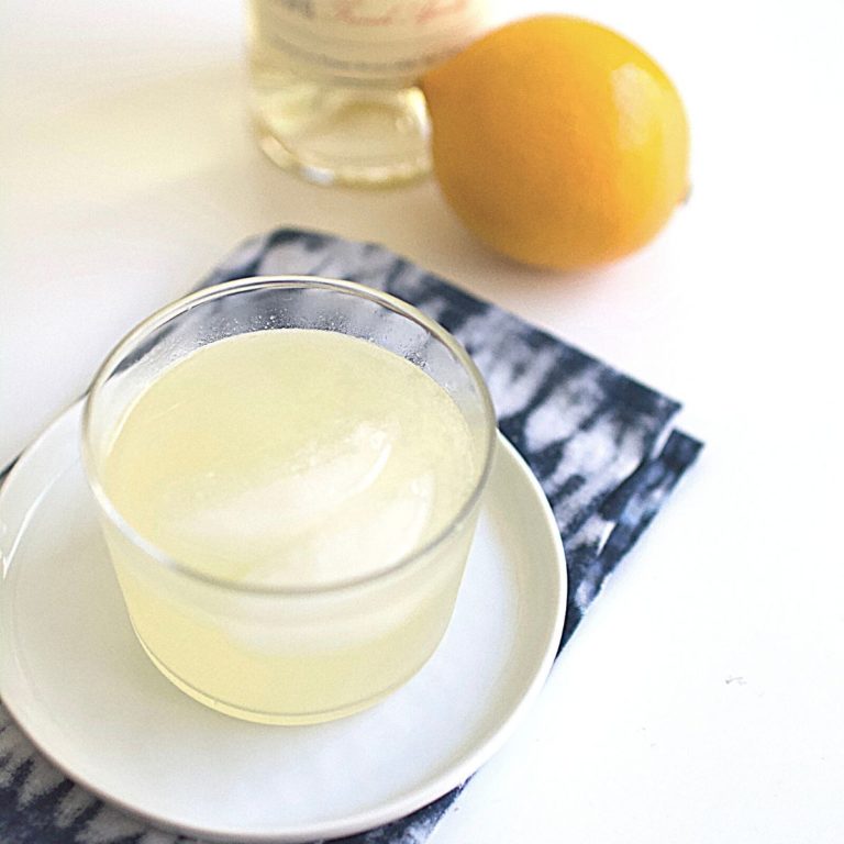 A corpse reviver cocktail next to a fresh lemon and a bottle of Lillet.