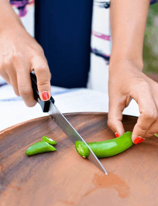 Woman slicing a serrano pepper on a wooden cutting board.