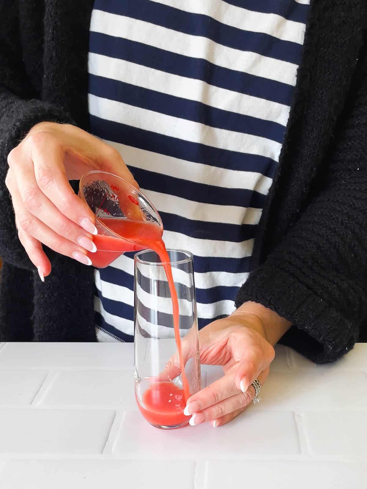 Woman pouring watermelon juice into a stemless champagne flute for a watermelon mimosa.