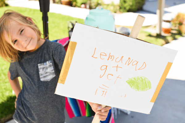 Kid holding a sign for a lemonade stand. 