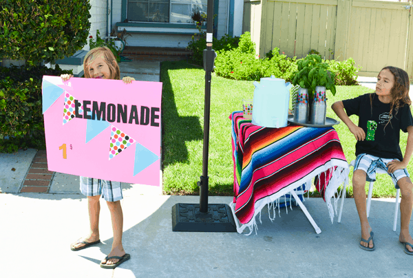 Kids in front of a lemonade stand. 