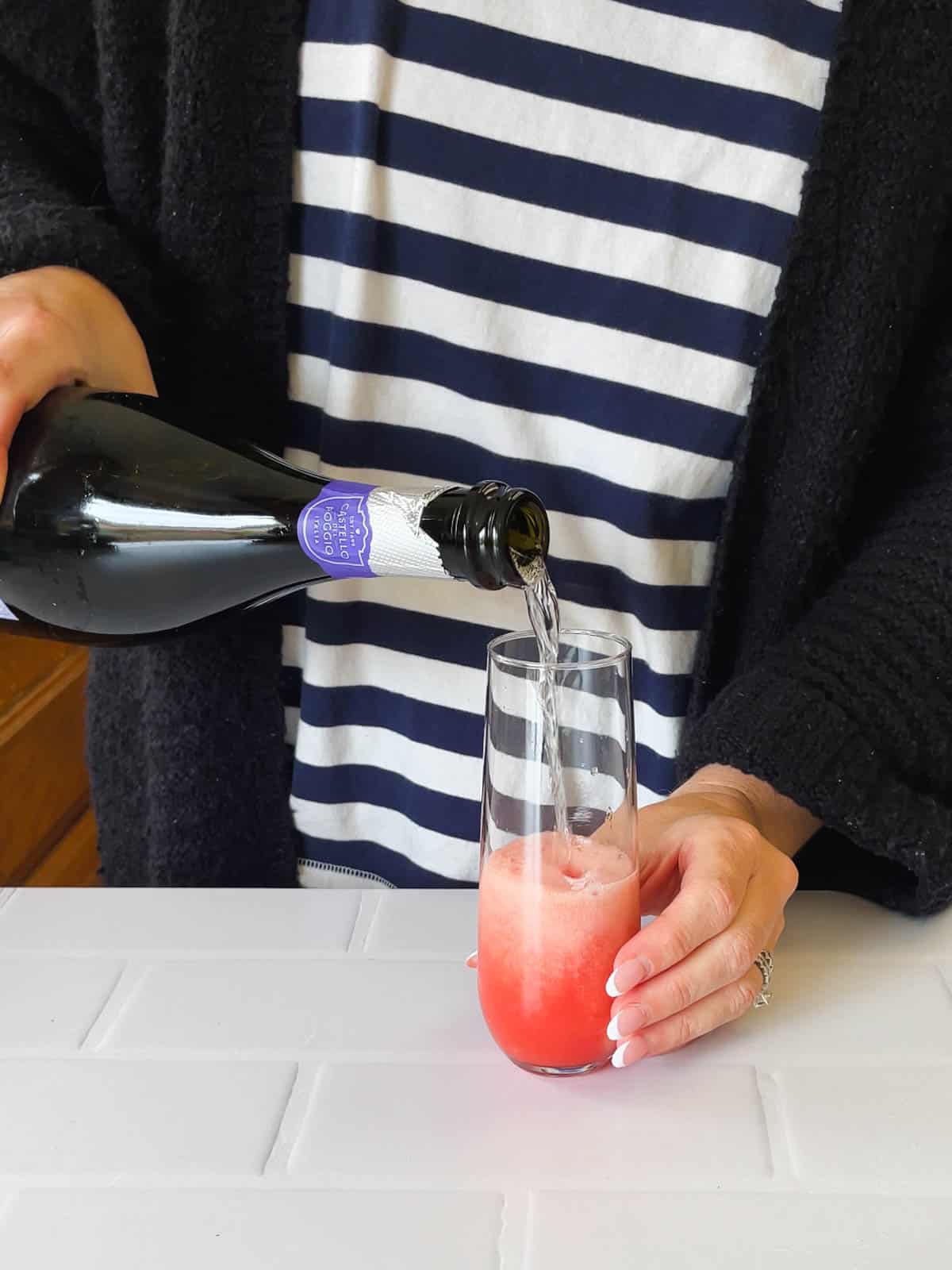 Woman adding champagne to watermelon juice in a glass for a mimosa.