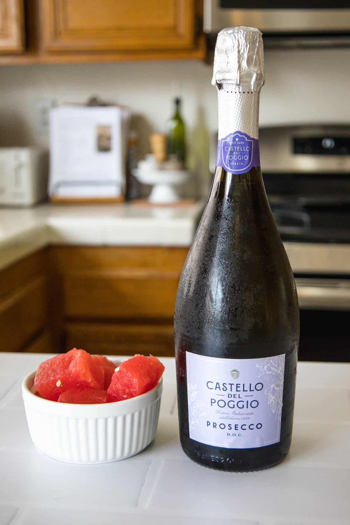 A small white bowl with fresh watermelon and champagne on a counter.