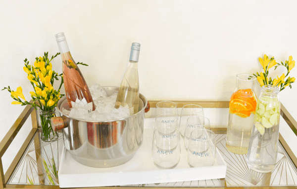 Wine bottles in a wine bucket on a bar cart next to some stemless wine glasses.