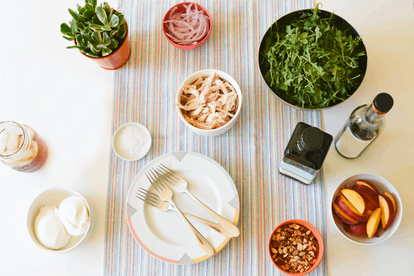 Ingredients in bowls on a table for each family member to build their own peach, arugula salad. 