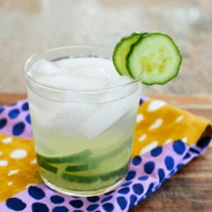 A short glass with a cocktail with muddled cucumbers, tequila and cactus water with a cucumber garnish.