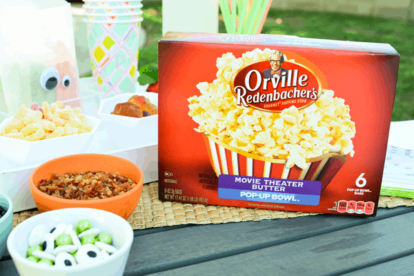 A box of microwave popcorn on a table next to other snacks. 