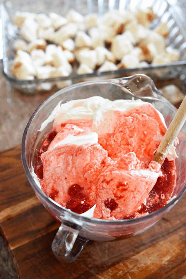 Angel food cake in a baking dish next to a bowl with frozen strawberries and Cool Whip.